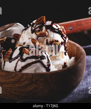 Libre de glace à la vanille garnie de sirop de chocolat et les pacanes dans un bol en bois sur fond sombre Banque D'Images