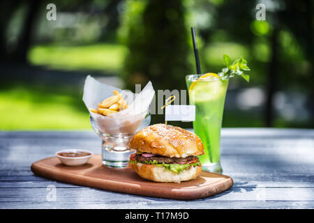 Burger de viande parfaite avec des frites et de la limonade fraîche. Sur la planche à découper, et l'été vert arrière-plan. Banque D'Images