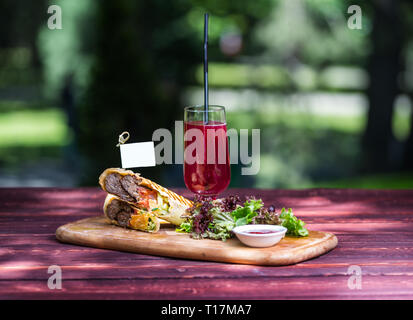 Sandwich shawarma sains à base de boeuf, salade verte, sauce et de la limonade. À la fine planche de bois, et l'été vert arrière-plan. Banque D'Images