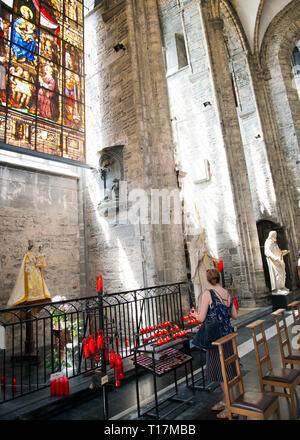 Femme éclairant des bougies à Small Alter, statue vierge Marie avec bébé Jésus, intérieur de l'église gothique Saint-Nicolas à Gand, Belgique Banque D'Images
