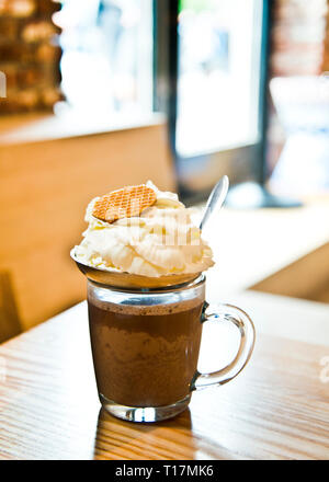 Un verre de chocolat chaud recouvert de crème fraîche et de biscuits ronds sur un fond de fenêtre légère, à l'intérieur. Banque D'Images