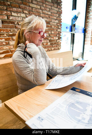 Femme d'âge moyen assise seule dans un café décontracté, regardant le menu dans un café moderne avec des meubles intérieurs de base Banque D'Images