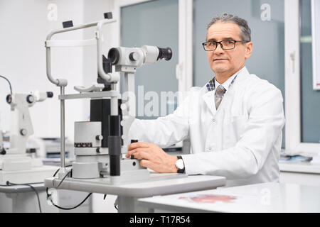 Médecin ophtalmologiste professionnel assis à table avec équipement spécial à la lampe à fente. Dispositif spécial pour l'examen de la vue des patients en clinique médicale. Concept de soins de santé et les tests de l'œil. Banque D'Images