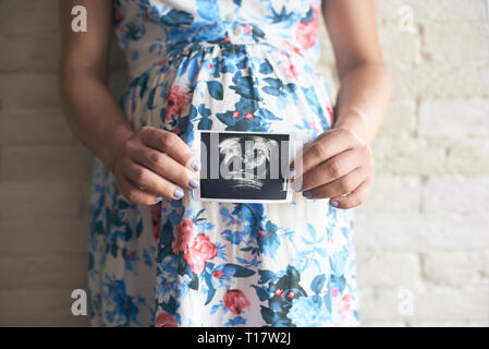 Femme enceinte avec gros ventre robe à fleurs en montrant l'image échographique de bébé. Avenir jeune mère attendre à peu enfant. Concept de la grossesse et Banque D'Images