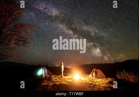 Nuit de camping paisible dans les montagnes. Jeune fille aux cheveux long touristique se tient entre deux tentes au camp de gravure profonde regarder ciel noir avec beaucoup de br Banque D'Images