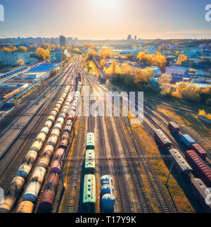 Vue aérienne de trains de marchandises colorées sur gare au coucher du soleil en automne. Wagons à marchandises sur le chemin de fer. L'industrie lourde. Scène industrielle avec ca Banque D'Images