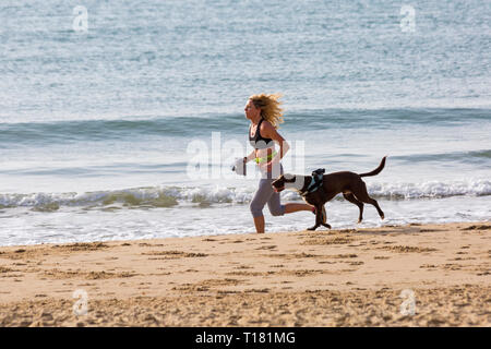 Bournemouth, Dorset, Royaume-Uni.24 mars 2019.Météo au Royaume-Uni : belle journée ensoleillée avec un ciel bleu et un soleil chaud sur les plages de Bournemouth, tandis que les visiteurs se rendent au bord de la mer pour profiter au maximum du temps glorieux.Femme en train de courir le long de la mer avec un chien.Crédit : Carolyn Jenkins/Alay Live News Banque D'Images