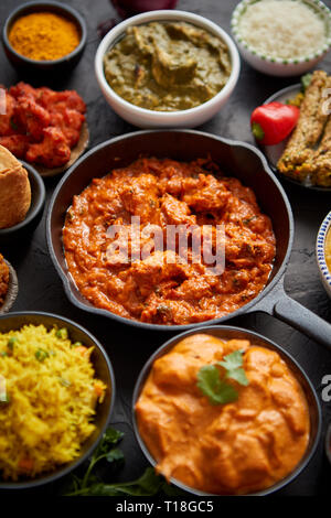 Divers plats indiens sur une table. Spicy chicken Tikka Masala dans la poêle de fer. Servi avec du riz, épices et naan. Ensemble d'autre genre nourriture indienne. Banque D'Images
