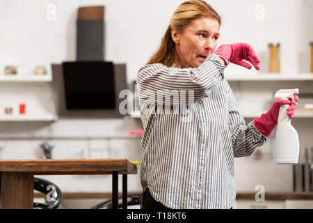 Porter des gants de ménagère chemise et nettoyer son appartement et de l'éternuement Banque D'Images