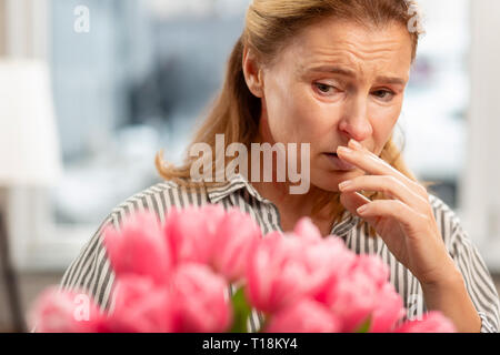 Femme d'âge mûr avec des rides du visage se sentir mal après avoir allergie aux tulipes Banque D'Images