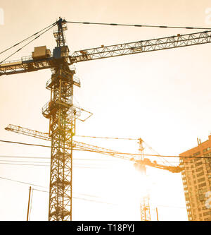 Site de construction avec des gratte-ciel en construction de bloc dans un environnement urbain dominé par une grande grue industrielle silhouetted against sunset sky Banque D'Images