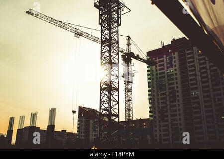 Site de construction avec des gratte-ciel en construction de bloc dans un environnement urbain dominé par une grande grue industrielle silhouetted against sunset sky Banque D'Images