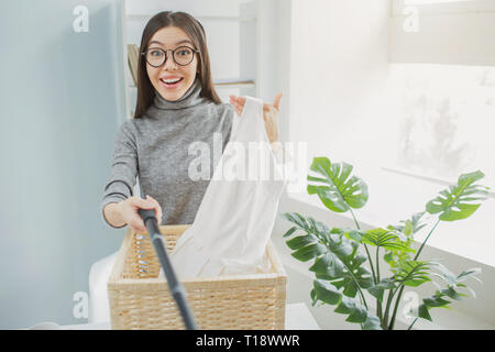 Heureux et belle fille est maintenant des vêtements blancs dans sa main et prendre des photos d'elle. Ces s'agit d'un panier de vêtements près de cette jeune fille. Jeune femme est s Banque D'Images