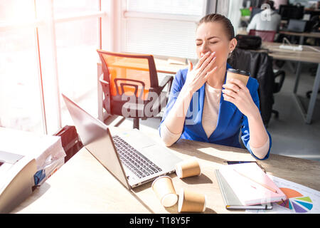 Femme d'affaires est assis près de la fenêtre. Elle s'ennuie. Cet adulte couvre sa bouche avec une main parce qu'elle bâille. Elle est fatiguée et que vous souhaitez obtenir de l'infiltrer Banque D'Images