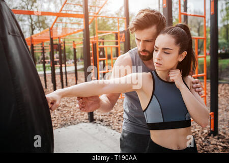 Les plus sportifs l'homme et la femme sont debout dans le parc et l'exercice ensemble. Jeune fille cherche à la boxe alors que son entraîneur est responsable de l'orientation de son se déplace Banque D'Images