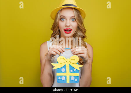 Très excitée fille est maintenant un cadeau bleu avec du jaune dans ses mains. Elle s'étonne beaucoup. Isolé sur fond jaune Banque D'Images