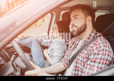 Une photo de Guy roulant en voiture sur la route. Il est à la 6e ligne droite la concentration. Jeune homme a l'air sérieux. Fille est assis en dehors de lui. Elle a Banque D'Images