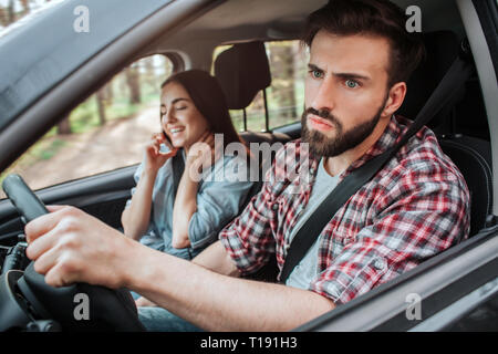 Les jeunes femmes est assis en plus d'homme qui est le moteur de voiture. Il est bouleversé et malheureux. Guy est à la recherche sur le côté avec sérieux. Banque D'Images