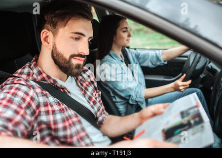 En plus, les gens sont équitation dans voiture. Fille est la conduite de la machine. Guy est assis à côté d'elle et la lecture d'un livre. Ils sont en voyage et passer du temps ensemble Banque D'Images