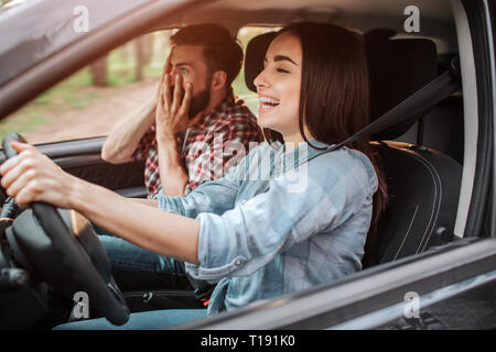 Girl est le moteur de voiture et rire. Guy est assis à côté d'elle. Il est terrifié à cause de sa petite amie de route. Jeune homme est couvrant son visage avec Banque D'Images