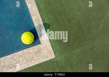 Balle de tennis jaune fluorescent dans le coin sur la surface en acrylique bleu Banque D'Images
