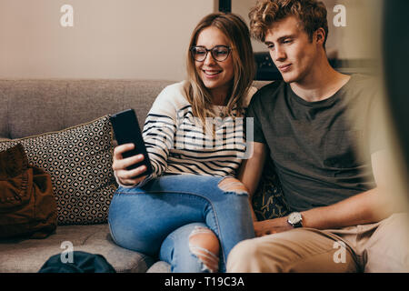 Deux étudiants en tenant avec selfies cellulaire au collège. Jeune homme et femme assise sur le canapé en prenant un autoportrait avec téléphone mobile. Banque D'Images