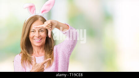 L'âge moyen femme brune portant des oreilles de lapin de Pâques sur fond isolé du châssis en souriant avec les mains et les doigts avec un visage heureux. La créativité Banque D'Images