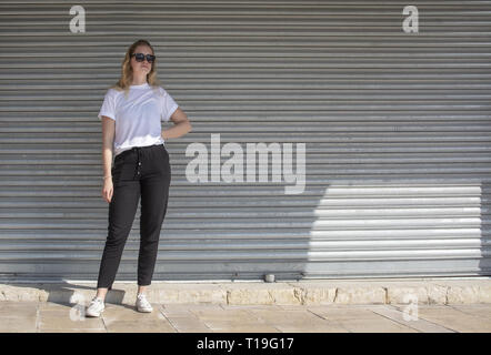 Corps plein photo de jeune femme blonde habillée sportive décontractée avec des lunettes en blanc T-shirt contre la tôle ondulée Wall street style ? Banque D'Images