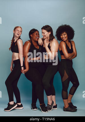 Groupe de femmes debout ensemble dans sportswear sur fond gris. Femme multi-ethnique de différentes tailles, smiling together. Banque D'Images