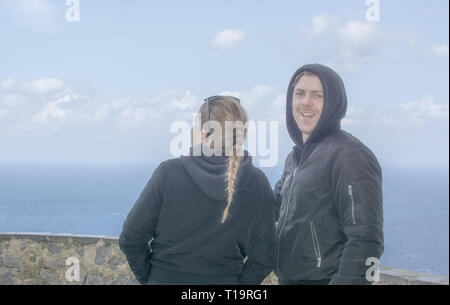 Beau jeune couple, habillé décontracté cheveux blonds tressés et capuche vestes, stand high par regarder dehors à la mer un jour de printemps à Mallorca, Espagne. Banque D'Images