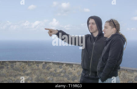 Jeune belle habillé décontracté couple stand haut pointant et en regardant vers la mer un jour de printemps à Mallorca, Espagne. Banque D'Images