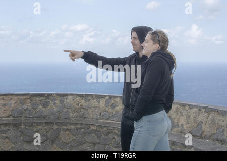 Jeune belle habillé décontracté couple stand haut pointant et en regardant vers la mer un jour de printemps à Mallorca, Espagne. Banque D'Images