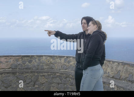 Jeune belle habillé décontracté couple stand haut pointant et en regardant vers la mer un jour de printemps à Mallorca, Espagne. Banque D'Images