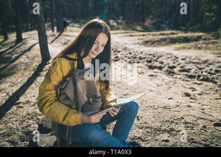 Style de voyage. Young woman traveler assis sur le moignon en bois avec une carte dans la forêt Banque D'Images