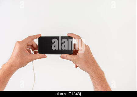 Holding phone dans l'orientation paysage à regarder du contenu en ligne (écran noir), point de vue image avec copie espace pour le texte. Banque D'Images