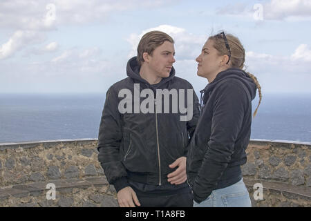 Jeune beau couple stand habillé décontracté tout en haut à la triste et grave par la mer par une froide journée de printemps à Mallorca, Espagne. Banque D'Images