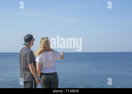 Jeune belle habillé décontracté couple stand haut pointant et en regardant vers la mer un jour de printemps à Mallorca, Espagne. Banque D'Images