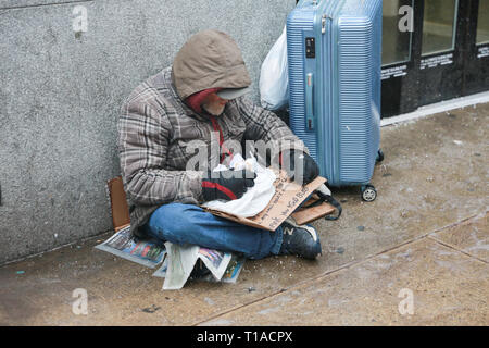 New York, NY - 12 Février 2019 : un sans-abri est de consommer des aliments, tout en maintenant un signe de l'aide, de l'alimentation, et de l'argent. midtown Manhattan. - Image Banque D'Images