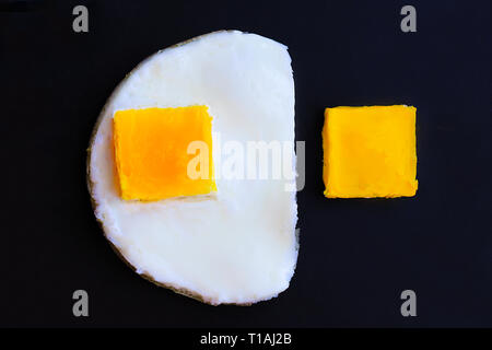 Oeufs au plat avec le jaune sous la forme d'un carré noir sur un poêle. Solution non standard. Banque D'Images