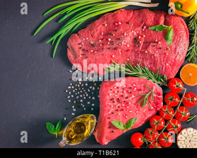 La viande crue. Steak de boeuf cru sur conseil sombre avec des herbes fraîches, légumes, condiments et épices. Vue de dessus ou de télévision. Copy space Banque D'Images