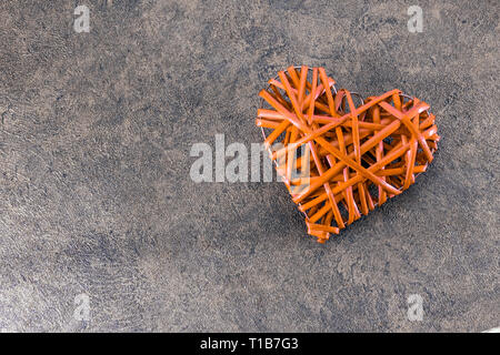 La paille en forme de coeur Orange tisser sur un fond texturé gris Banque D'Images