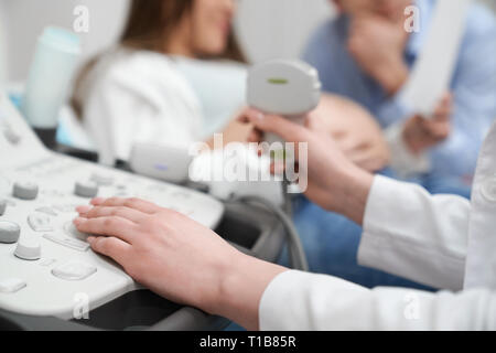 Doctor holding device, main sur échographe close up. Pregnant woman lying on examen échographie de l'abdomen. Clinique médicale moderne et professionnelle. Banque D'Images