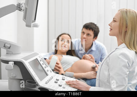 Future mère et père sur la consultation avec un médecin, de faire un examen échographique, à surveiller, à de la machine. Femme médecin faisant à l'aide de l'échographie de l'appareil moderne dans une clinique médicale. Banque D'Images