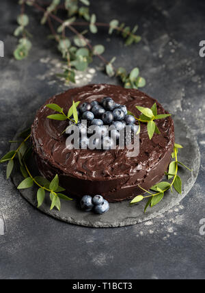 Gâteau au chocolat élégant avec des bleuets et de feuilles vertes sur fond gris foncé. Concept de délicieux aliments de vacances Banque D'Images