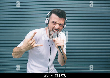 Cool est debout et poser sur l'appareil-photo. Il hurle au mic et montrant le signe cool. Homme porte un casque. Il est à l'écoute de la musique. Isolé Banque D'Images