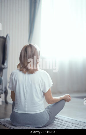 Une femme adulte médite après avoir fait du Yoga à la maison dans le salon. Banque D'Images