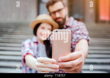 Photo de couple holding phone ensemble et le regarder. Ils sourient. Les touristes se tenir en face de l'escalier. Qu'ils posent. Banque D'Images