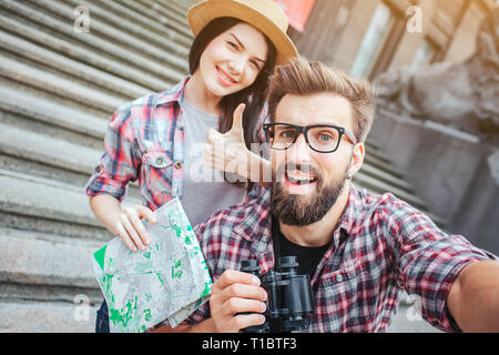 Heureux et excité les touristes dans les escaliers et se poser sur l'appareil-photo. Jeune homme barbu tient. Elle montre big thumb up et garde la carte en main. Banque D'Images