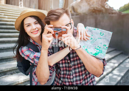 Heureux les touristes se tiennent à l'extérieur et la pose. Elle sourit et embrasser son petit ami. Il prend des photos par tenir l'appareil photo en mains. Carte de touriste a femelle Banque D'Images