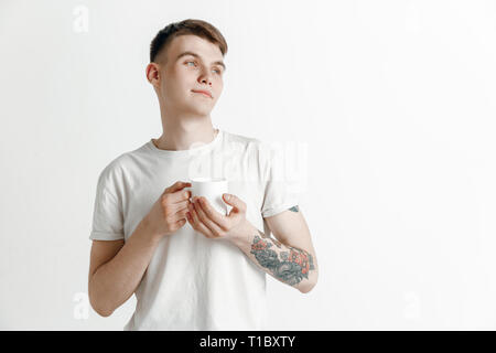 Prendre une pause-café. Handsome young man holding Coffee cup, souriant alors que l'article contre l'arrière-plan gris studio Banque D'Images